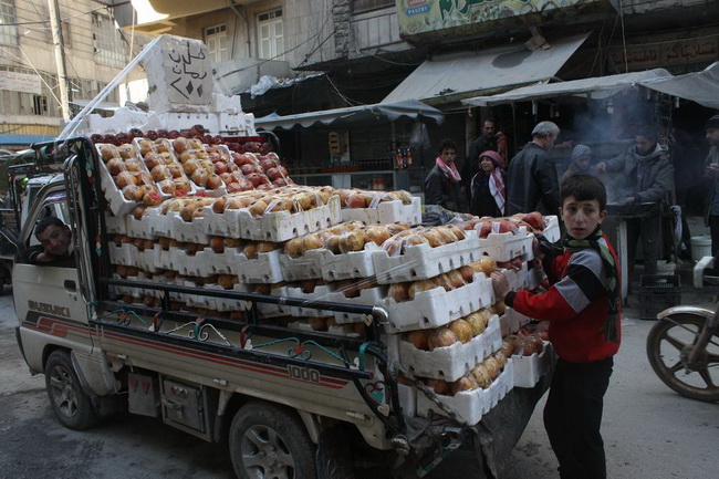 Ребенок стоит около ящиков с гранатами, которые он продает в Алеппо, у него остаются излишки товара, потому что очень много людей покинуло некогда шумную торговую столицу страны.
