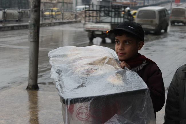 Ребенок продает пирожки с лотка на улице в Алеппо, он работает под холодным дождем.