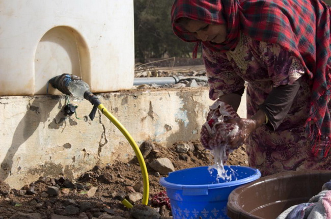 Женщина стирает белье, среди грязи, используя для этого воду из ближайшей реки.