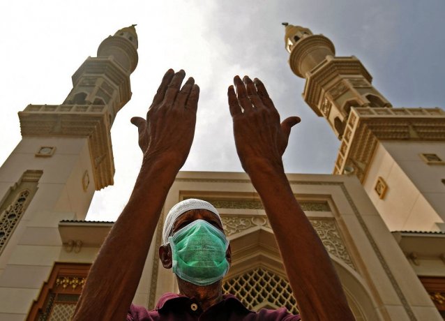 Пожилой мужчина  маске молится возле мечети, которая была закрыта для верующих во время пандемии коронавируса, в Шарджа, ОАЭ.